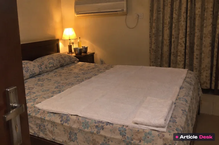 A bed made ready for a massage, with a big towel on the sheet and a soft bedside lamp on