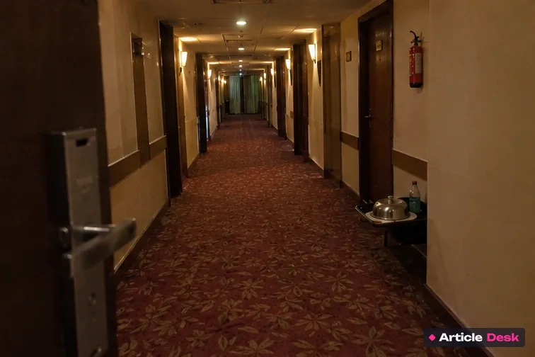 An empty hotel corridor seen from an open room door, with nobody coming